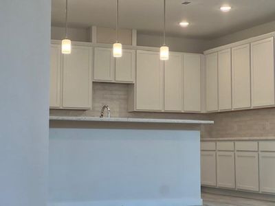 Kitchen with light wood-type flooring, pendant lighting, white cabinets, and decorative backsplash