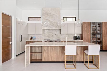 From this view of the gourmet kitchen, you will notice the exquisite Taj Mahal quartzite vent hood and matching backsplash. Above the sleek custom Madeval cabinetry, transom windows allow natural light to filter in, enhancing the bright and open feel of the space.