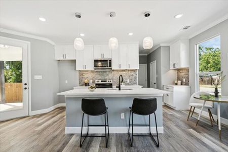 Kitchen with decorative light fixtures, stainless steel appliances, light wood-type flooring, and white cabinets