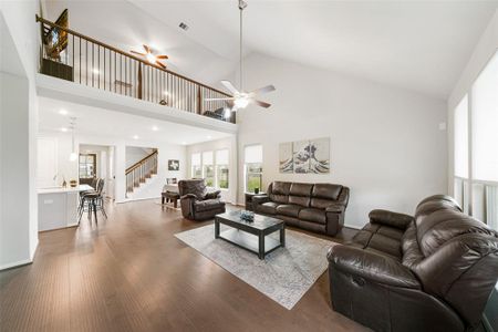 This is a spacious, open-concept living room with high ceilings, ample natural light, and a second-floor balcony overlooking the area. It features hardwood floors and is adjacent to a dining space and kitchen, ideal for modern living.