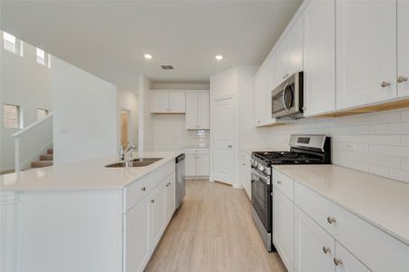 Kitchen featuring white cabinetry, light hardwood / wood-style flooring, appliances with stainless steel finishes, sink, and a center island with sink