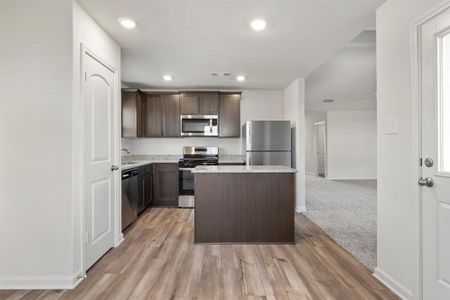 Kitchen with a center island, stainless steel appliances, light carpet, dark brown cabinets, and sink