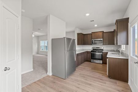 Kitchen featuring appliances with stainless steel finishes, light stone counters, light carpet, sink, and dark brown cabinetry