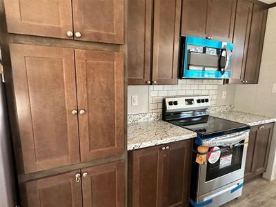 Kitchen featuring hardwood / wood-style floors, stainless steel appliances, light stone counters, and backsplash