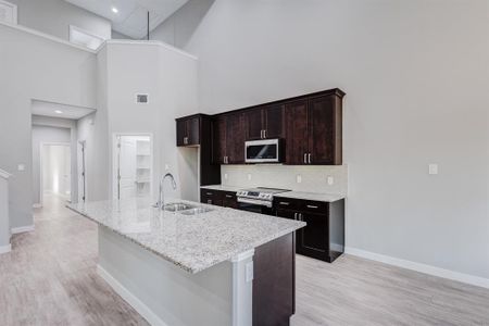 Kitchen featuring appliances with stainless steel finishes, light hardwood / wood-style flooring, sink, decorative backsplash, and a towering ceiling