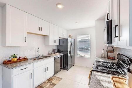 Kitchen featuring light stone countertops, stainless steel appliances, sink, white cabinetry, and light tile patterned floors