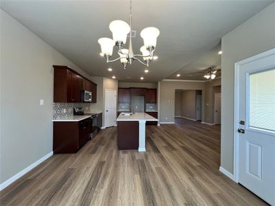 Kitchen with dark wood-type flooring, sink, ceiling fan with notable chandelier, decorative backsplash, and appliances with stainless steel finishes