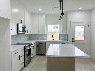 Kitchen featuring white cabinetry, stainless steel appliances, a wealth of natural light, and hanging light fixtures