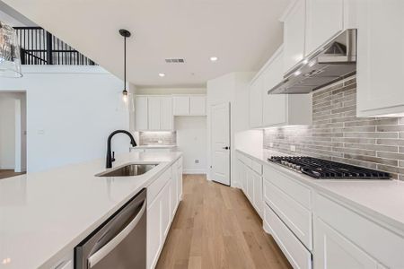 Kitchen featuring stainless steel appliances, white cabinets, light hardwood / wood-style floors, and wall chimney range hood