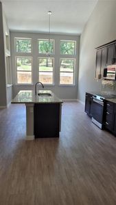 Kitchen featuring dark wood-type flooring, light stone counters, decorative backsplash, stove, and sink