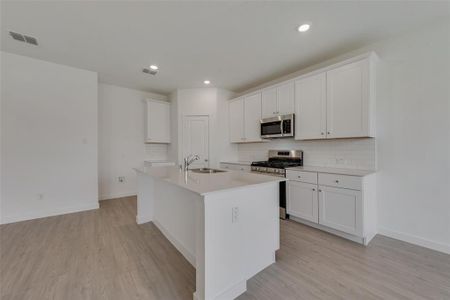 Kitchen featuring white cabinets, light hardwood / wood-style flooring, stainless steel appliances, sink, and a kitchen island with sink