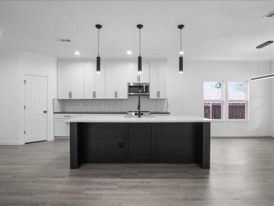 Kitchen with hardwood / wood-style flooring, decorative light fixtures, white cabinets, and an island with sink