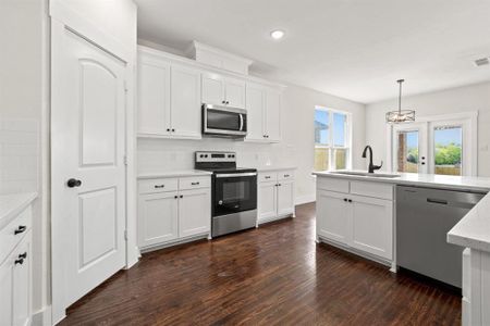 Kitchen with appliances with stainless steel finishes, white cabinetry, dark hardwood / wood-style flooring, decorative light fixtures, and sink