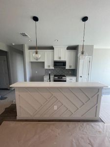 Kitchen with electric range, white cabinetry, decorative backsplash, decorative light fixtures, and a spacious island