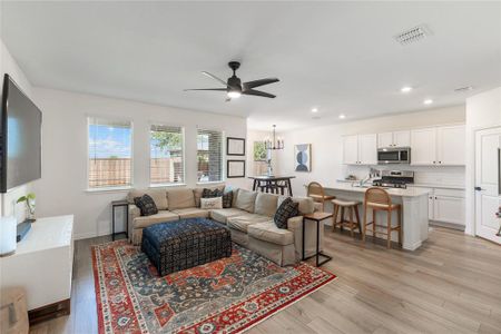 Living room with ceiling fan with notable chandelier and light hardwood / wood-style floors