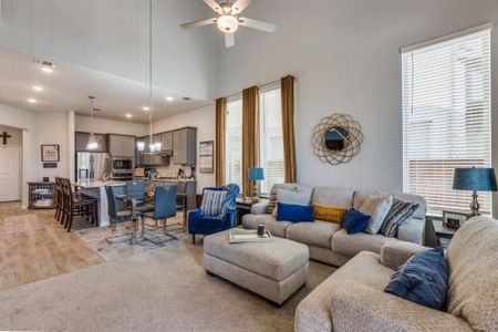 Living room with ceiling fan, a towering ceiling, and light colored carpet