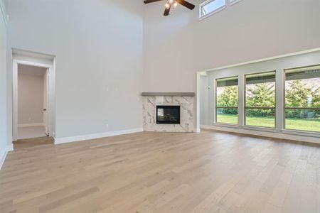 Unfurnished living room with a towering ceiling, light hardwood / wood-style flooring, a premium fireplace, and ceiling fan