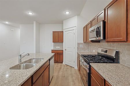 Kitchen featuring appliances with stainless steel finishes, sink, backsplash, light hardwood / wood-style floors, and light stone counters