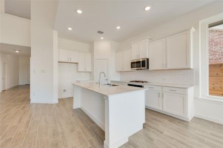 Kitchen with white cabinets, a center island with sink, sink, and light wood-type flooring