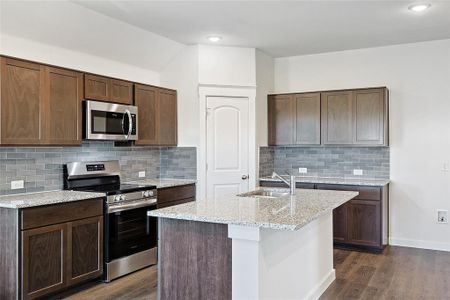 Kitchen featuring a kitchen island with sink, dark wood-type flooring, stainless steel appliances, sink, and decorative backsplash