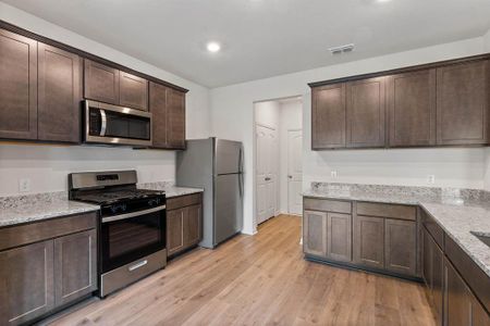 Kitchen featuring light wood-style flooring, stainless steel appliances, light stone counters, and dark cabinets