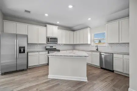 The kitchen features plenty of storage with Island and breakfast bar, 42" upper cabinets, stainless steel appliances, and stylish tile backsplash.