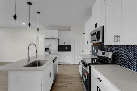 Kitchen with appliances with stainless steel finishes, hanging light fixtures, white cabinets, a kitchen island with sink, and sink