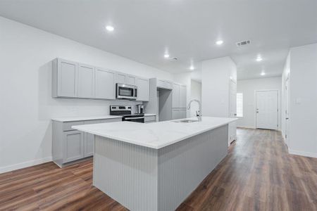 Kitchen featuring dark wood-type flooring, light stone counters, stainless steel appliances, and a center island with sink