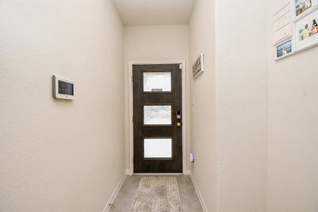This is a well-lit entryway featuring a modern front door with glass panels, a neutral color palette and tiled flooring.