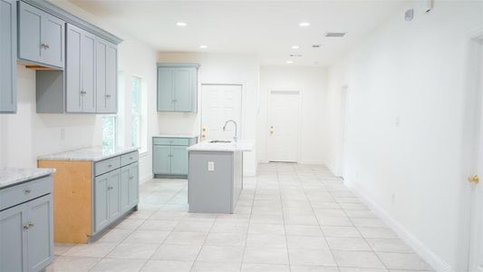 Kitchen featuring light tile patterned floors, light stone counters, a kitchen island with sink, and sink