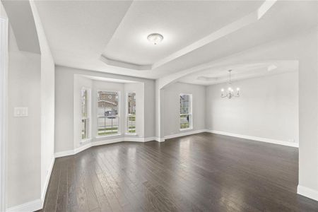 Unfurnished living room with an inviting chandelier, a raised ceiling, dark hardwood / wood-style flooring, and plenty of natural light