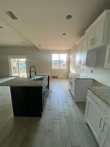 Kitchen featuring backsplash, sink, an island with sink, a wealth of natural light, and white cabinetry