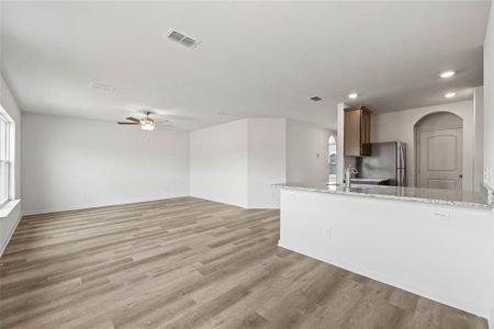 Kitchen with sink, light wood-type flooring, ceiling fan, light stone counters, and stainless steel refrigerator