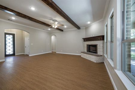 Unfurnished living room featuring ornamental molding, beam ceiling, ceiling fan, and dark wood-type flooring