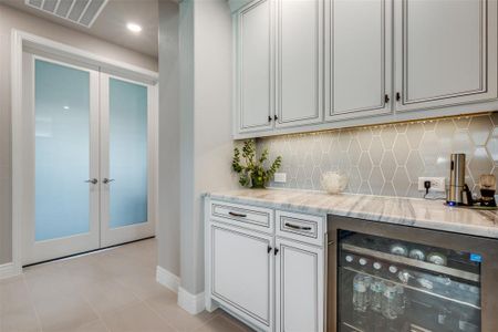 Bar with light tile patterned floors, beverage cooler, light stone countertops, and tasteful backsplash