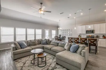 Living room with ceiling fan, LVP-type flooring, high 11' sloped ceiling, and view of kitchen