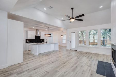 Kitchen with light wood-type flooring, white cabinets, pendant lighting, wall chimney range hood, and a center island with sink