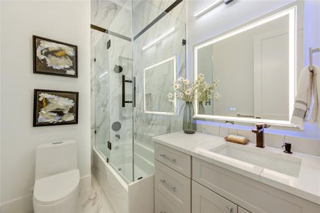 This Full Bath on the Hallway has Colorful LED Mirror, Glass Enclosure tub and Floor-Ceiling Porcelain Tile