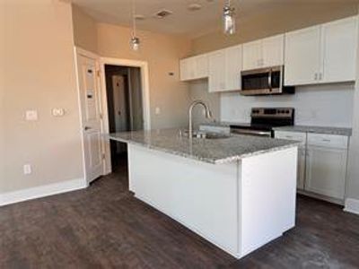 Kitchen featuring a kitchen island with sink, sink, white cabinets, stainless steel appliances, and decorative light fixtures