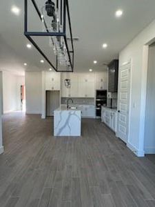 Kitchen featuring white cabinets, a kitchen island with sink, and dark wood-type flooring