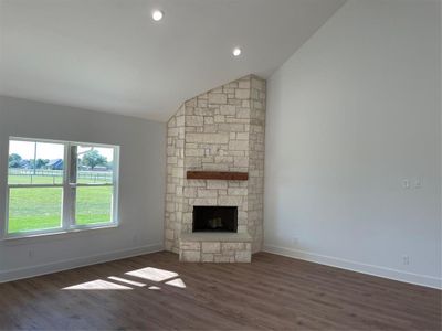 Unfurnished living room featuring dark hardwood / wood-style floors, a stone fireplace, and lofted ceiling