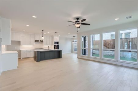 Kitchen featuring an island with sink, hanging light fixtures, ceiling fan, white cabinets, and light hardwood / wood-style flooring