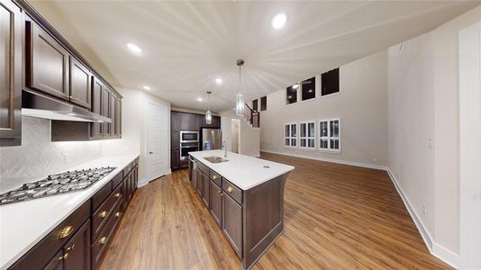 Kitchen featuring stainless steel appliances, a center island with sink, decorative light fixtures, light hardwood / wood-style floors, and tasteful backsplash