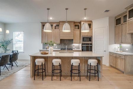 Kitchen featuring light hardwood flooring, a kitchen island with leathered Quartzite countertops, farm sink, natural stain custom cabinetry with soft close drawers and cabinets.