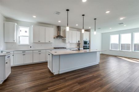 Kitchen featuring dark wood-type flooring, wall chimney exhaust hood, and a kitchen island with sink