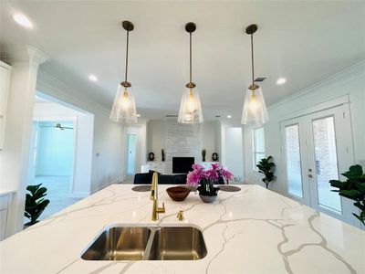 Kitchen with sink, light stone countertops, pendant lighting, and crown molding
