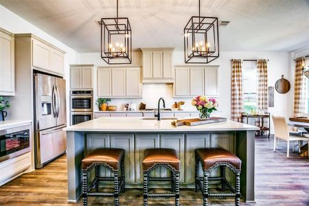 Kitchen with appliances with stainless steel finishes, hanging light fixtures, light hardwood / wood-style flooring, and an island with sink