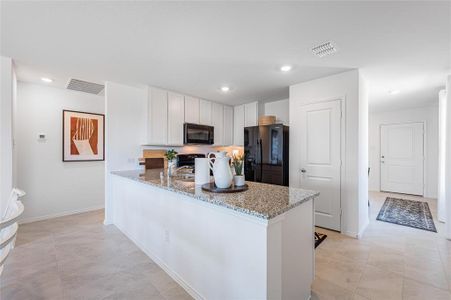 Kitchen with black appliances, white cabinets, kitchen peninsula, light stone countertops, and light tile patterned flooring