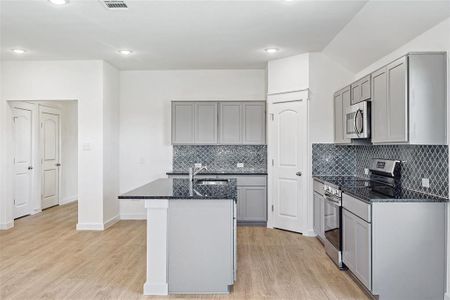 Kitchen featuring a kitchen island with sink, stainless steel appliances, gray cabinetry, and light hardwood / wood-style floors