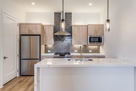 Kitchen featuring light stone counters, light hardwood / wood-style flooring, stainless steel appliances, sink, and pendant lighting